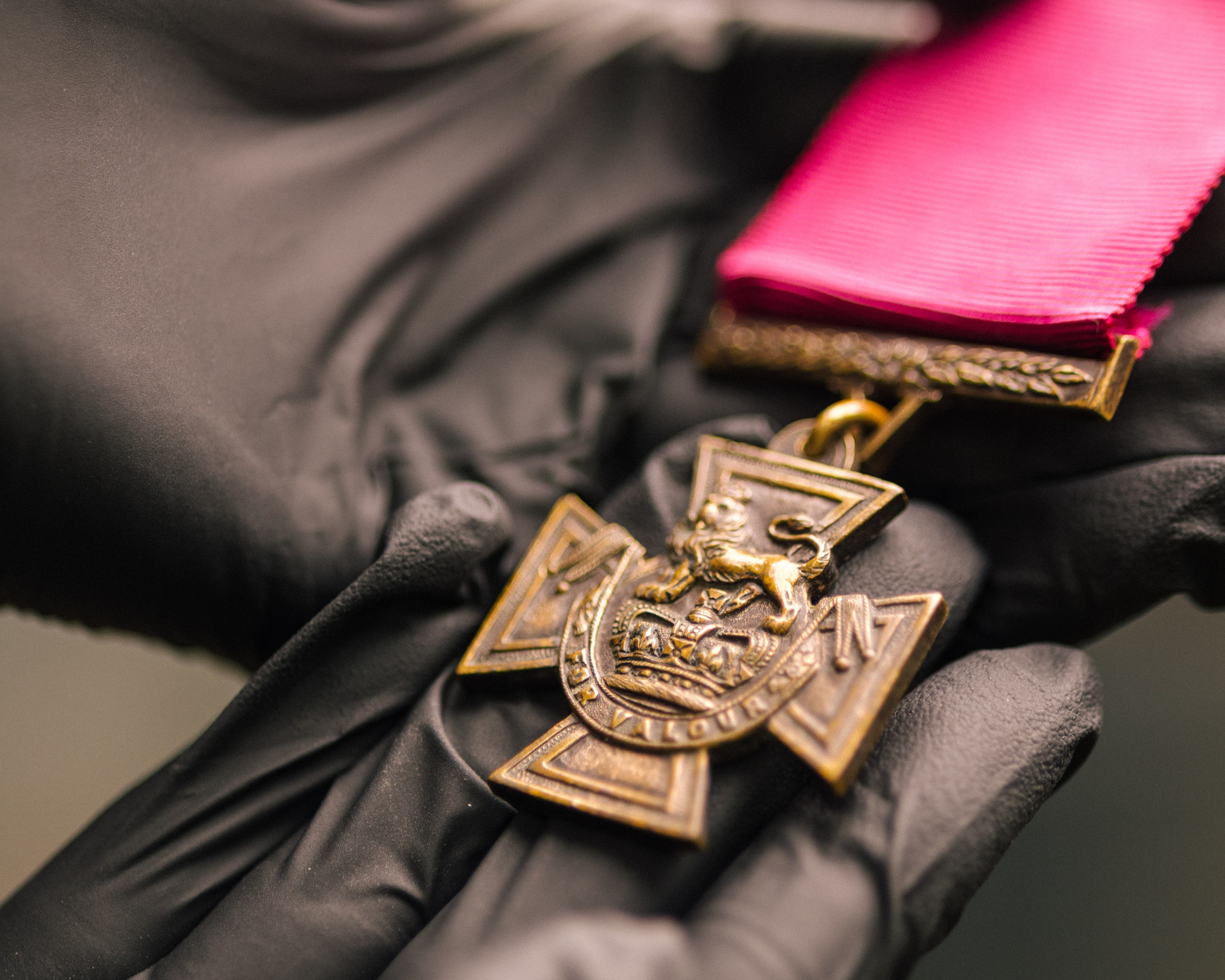 Curator in black gloves holding a Victoria Cross medal with crimson ribbon, at the Royal Marines Museum