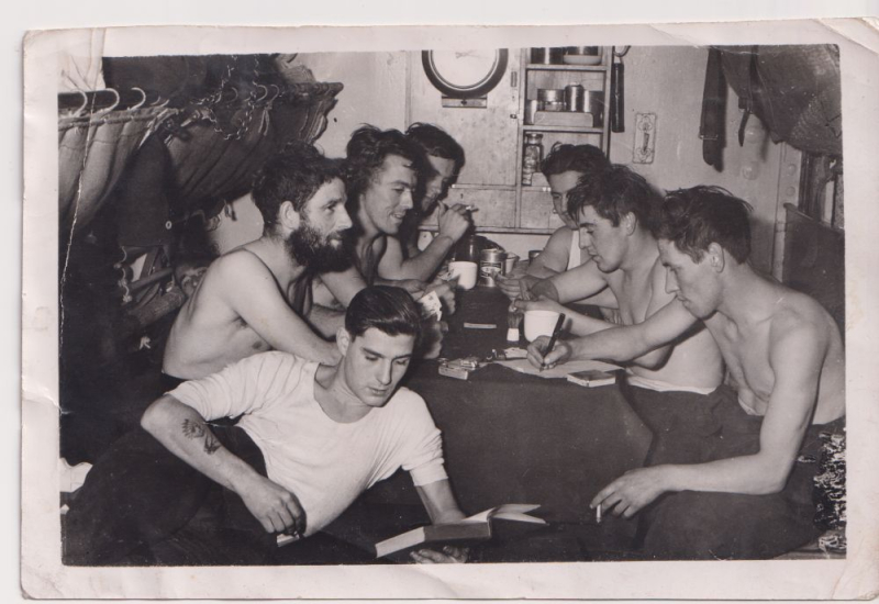 Seven men gathered around a small table onboard HMS Alliance. 