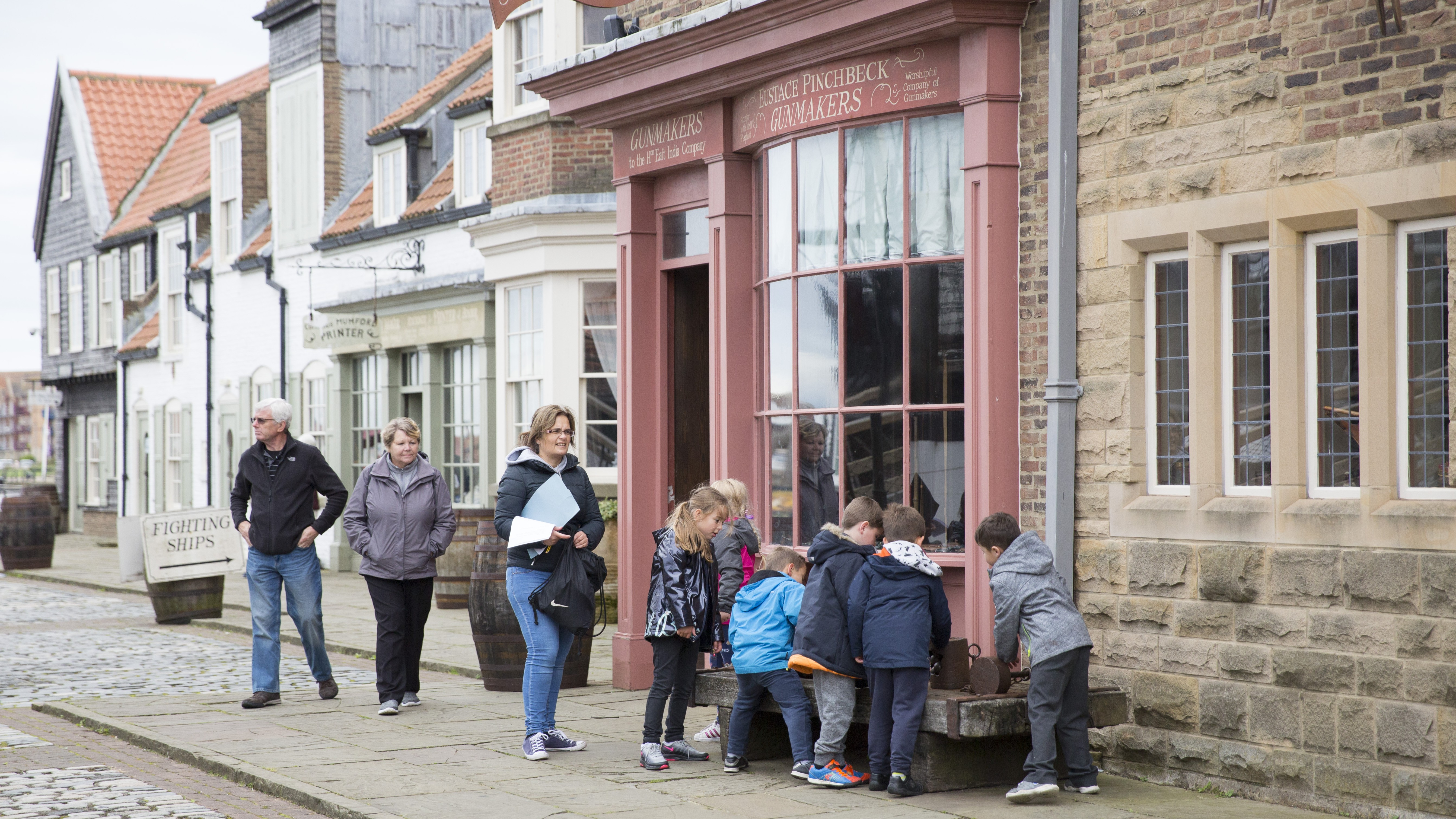 Visitors and a group of children explore a recreated Georgian street at Royal Navy Museums: Hartlepool, with a period gunmaker's shopfront visible