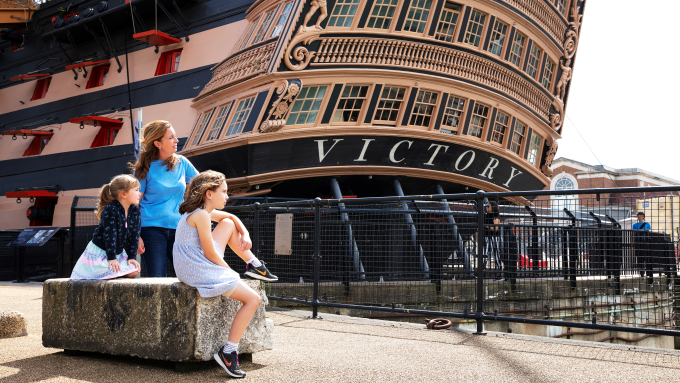 Family sitting in front of HMS Victory's stern at Portsmouth Historic Dockyard.