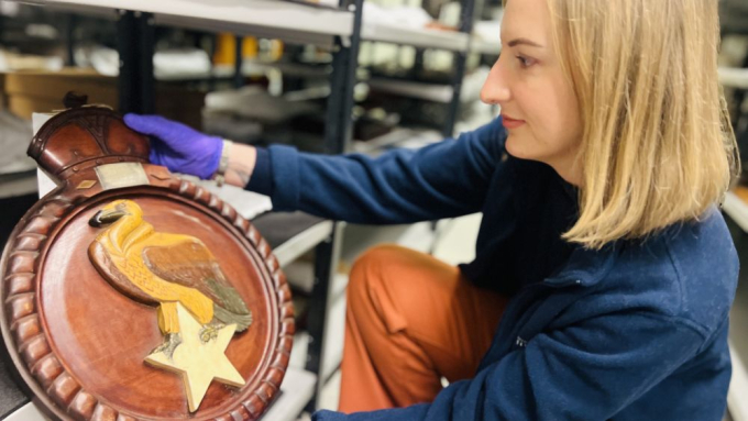 A curator removing a ship's badge from our collection shelves. 