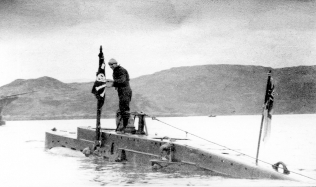 The submarine x24 surfacing above the water with a crew member standing on it's top. 