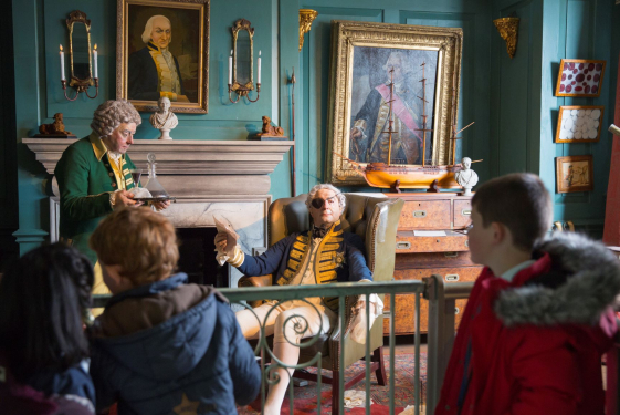 A group of school children looking at a recreation of a Georgian Officer relaxing. 