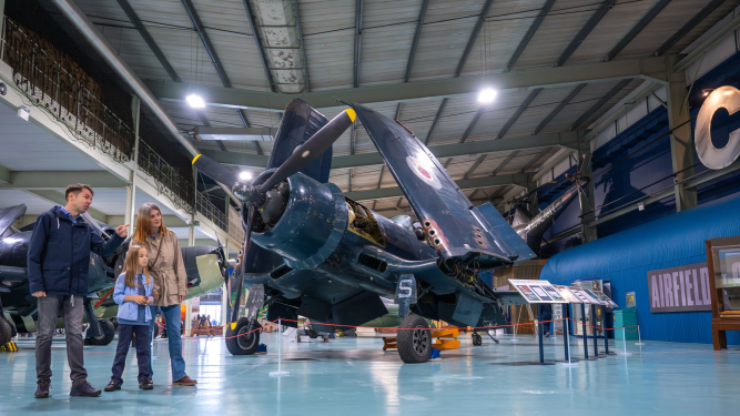 Family standing next to a Second World War plane with it's wings folded. 