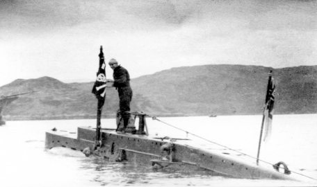 The submarine x24 surfacing above the water with a crew member standing on it's top. 