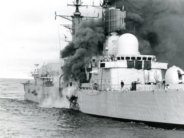 A Royal Naval destroyer with smoke billowing out of it from an attack.