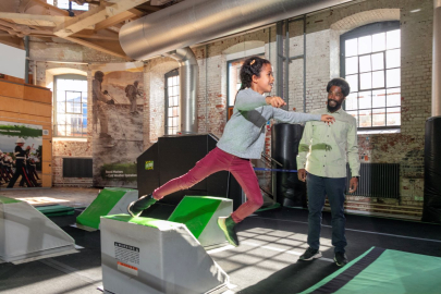 Young girl uses the obstacle course at Action Stations as her father watches. 