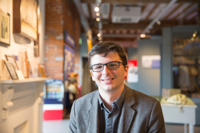 Andrew Baines smiles facing the camera with a museum gallery in the background.