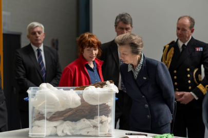Princess Anne looking at historical artefacts with naval officers behind her. 