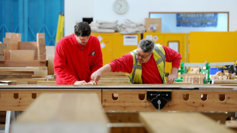 Two shipwrights woodworking in their workshop.  