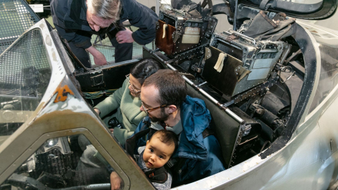 Parents and baby sit in a aircraft cockpit at the Fleet Air Arm Museum.  