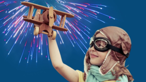 A little boy wearing aviator googles and holding up a toy plane. 