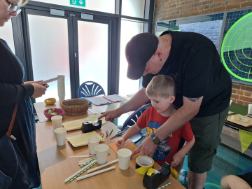 A man and boy look at craft materials laid out across a table.