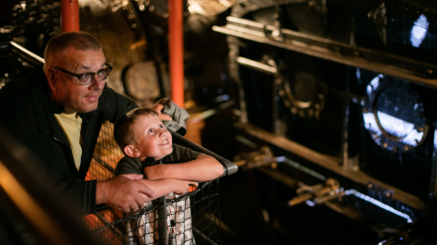 A young boy and older man looking in awe at the engine room in Royal Navy Museums: HMS Caroline