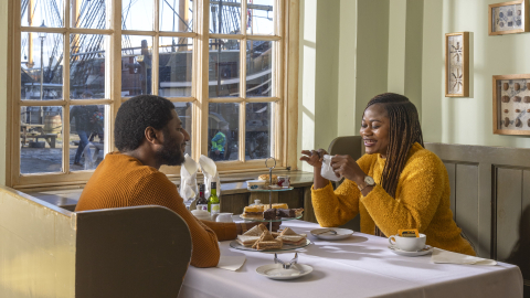 A couple enjoying afternoon tea at the Quayside Café at Royal Navy Museums: Hartlepool, with HMS Trincomalee's masts and rigging visible through the window behind