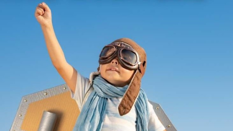 Image of a child in pilot goggles and cardboard wings, arm raised