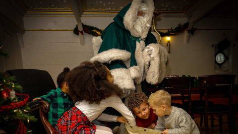 Children looking into a sack with a costumed figure in a green fur-trimmed cloak at a Christmas Ship event