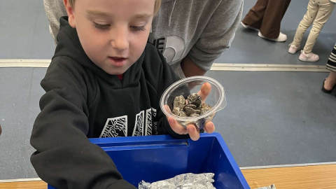 A child holding a pot of stones over a tray of water during 'Little Steamers: Float My Boat'