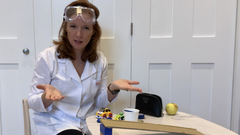 Presenter in a lab coat and safety goggles demonstrating a ramp experiment with toy cars for 'Little Steamers: Marvellous Machines'