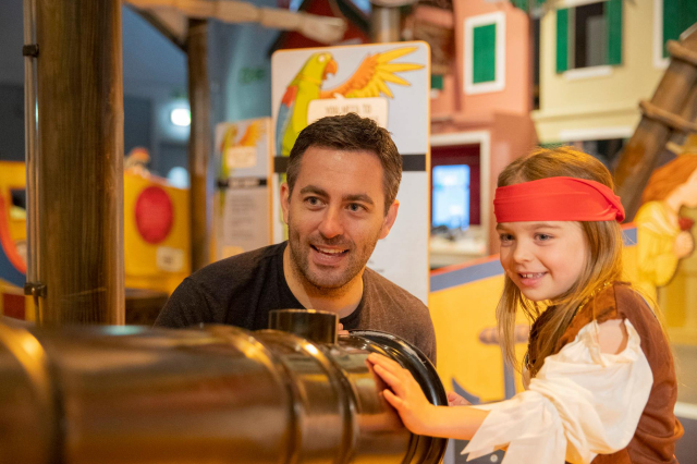A father and daughter play with a toy ship gun.