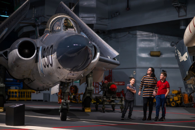 Mother and sons look up at a Royal Navy aircraft housed at the Fleet Air Arm Museum.