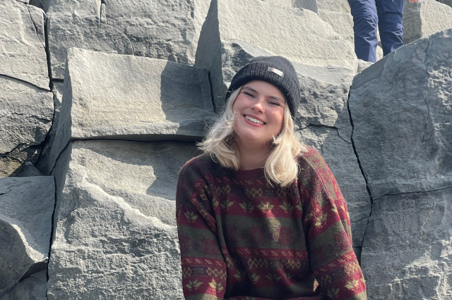 A young white woman with blonde hair sitting in front of some rocks. 