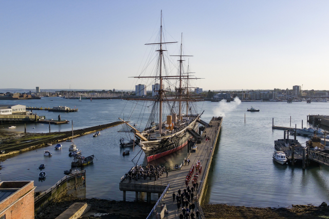 Drone shot of HMS Warrior at dock in Portsmouth Harbour surrounding by small civilian craft. 