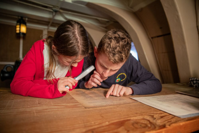 A child holding a magnifying glass looking at an old letter. 