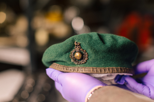 Curator in purple gloves holding a Royal Marines green beret with globe and laurel cap badge