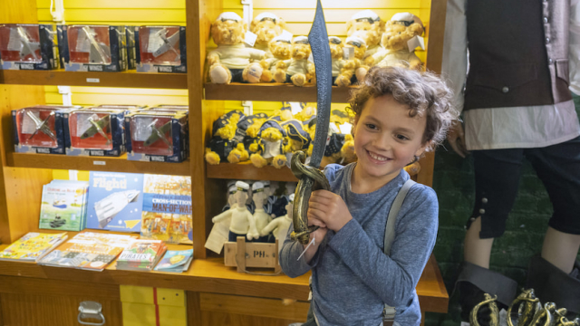 A young boy holds up a toy sword in a National Museum of the Royal Navy gift shop. 