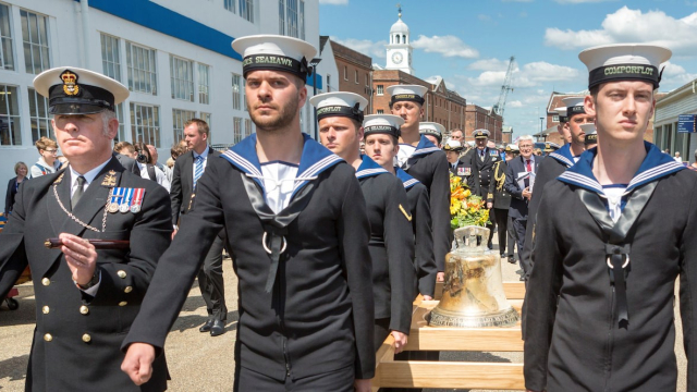 Royal naval personnel solemnly carrying the bell of HMS Hood through Portsmouth Historic Dockyard.  