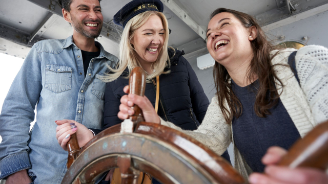 Three people laughing in a ship's wheelhouse. 