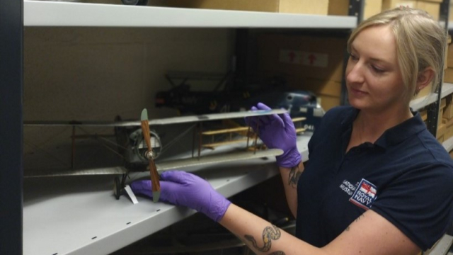 A conservator holding a model of a small biplane. 
