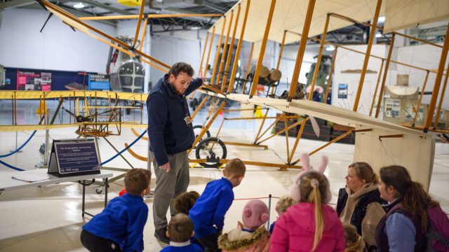 A team member from the Fleet Air Arm Museum show a group of children a bi-plane. 