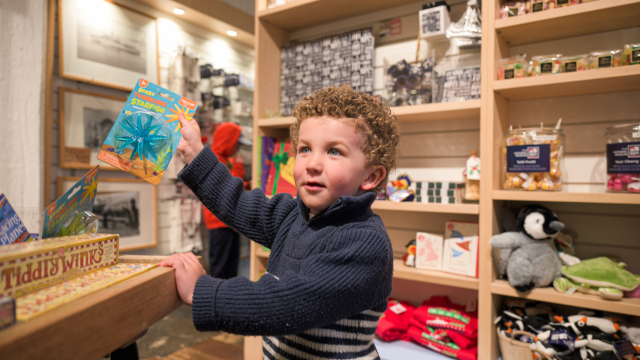 A small child holding up a book in the gift shop. 