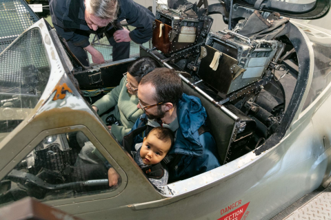 Couple with baby sits in a airplane cockpit. 