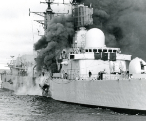 A Royal Naval destroyer with smoke billowing out of it from an attack.