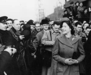 A young Queen Elizabeth visiting a Naval base surrounded by Naval officers and press. 