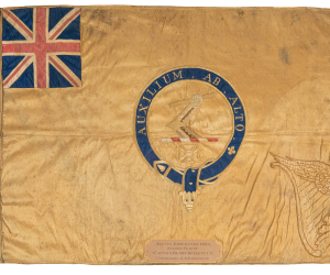 A beige flag with a Union Jack on the top left corner and a Latin inscription in the centre.  
