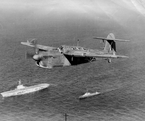 A Fairey Barracuda flying over battle cruisers at sea. 