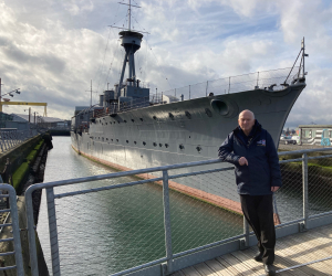 John Taylor, who served onboard HMS Caroline as an engineer, pictured infront of the ship