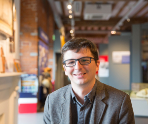 Andrew Baines smiles facing the camera with a museum gallery in the background.