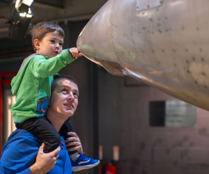son on fathers shoulders inspecting nose of plane