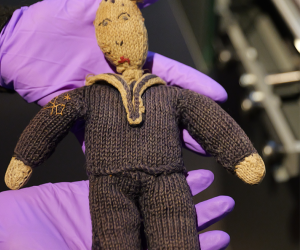A knitted toy in the shape of sailor being held in purple gloves