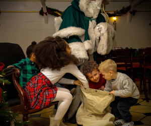 Children looking into a sack with a costumed figure in a green fur-trimmed cloak at a Christmas Ship event