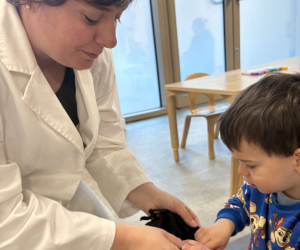 A child reaches into a small bag held by a lab-coated presenter during 'Little Steamers: Coding Unplugged