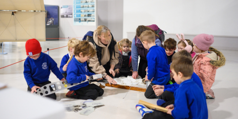 A group of infant school children looking at an original ship building tool.