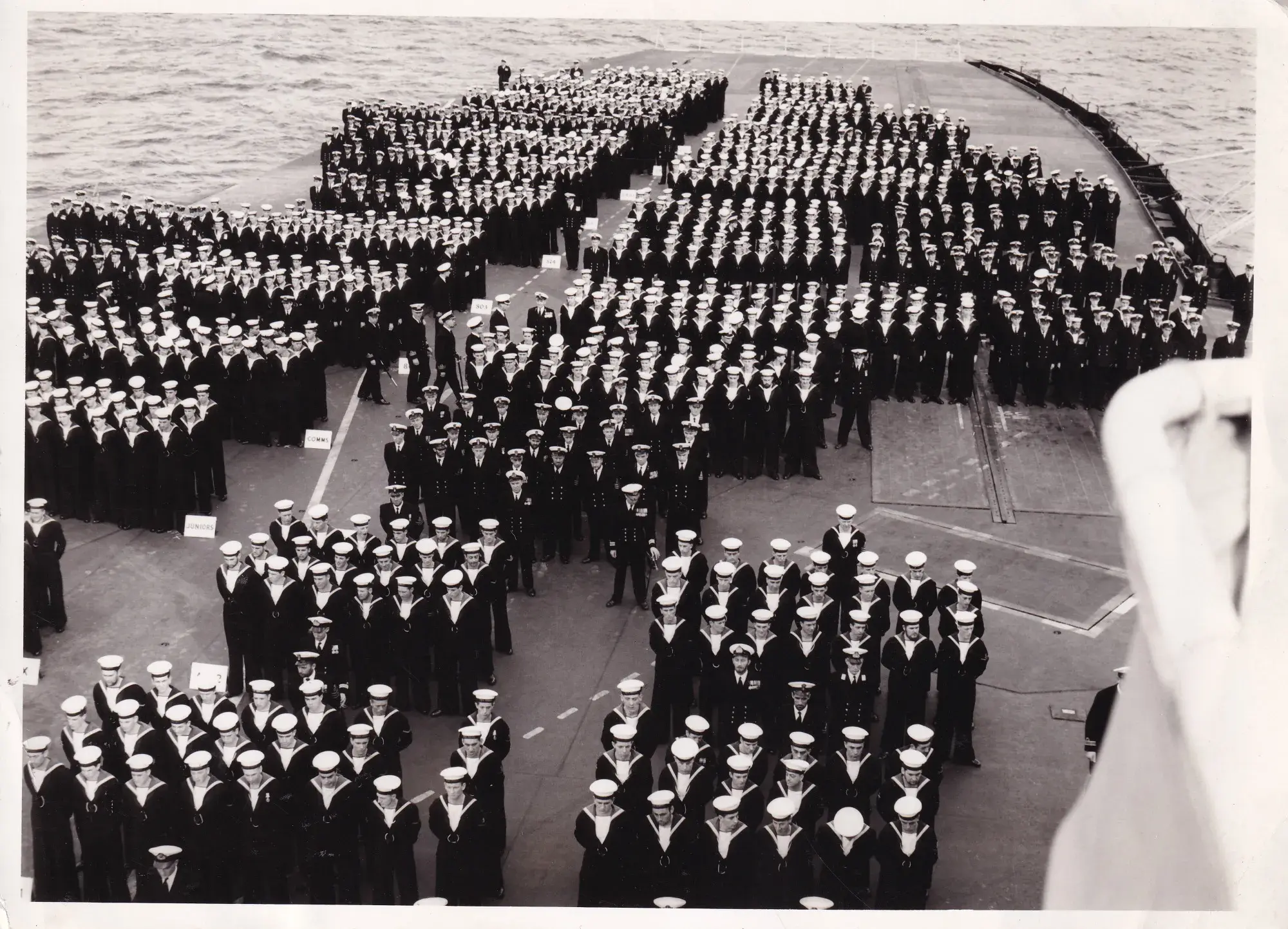 Naval personnel standing in formation on the top deck of a battle ship. 