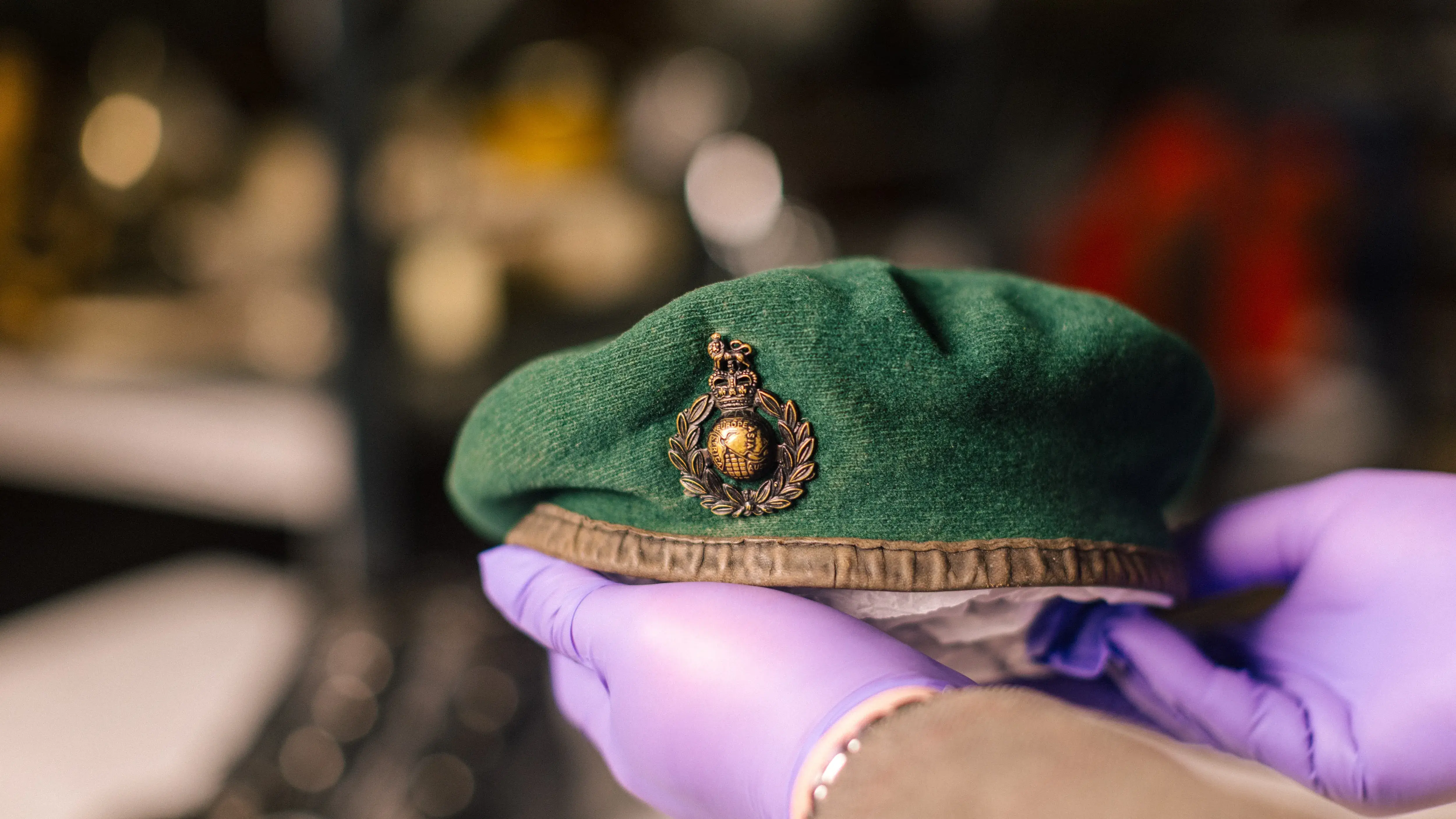 Curator in purple gloves holding a Royal Marines green beret with globe and laurel cap badge